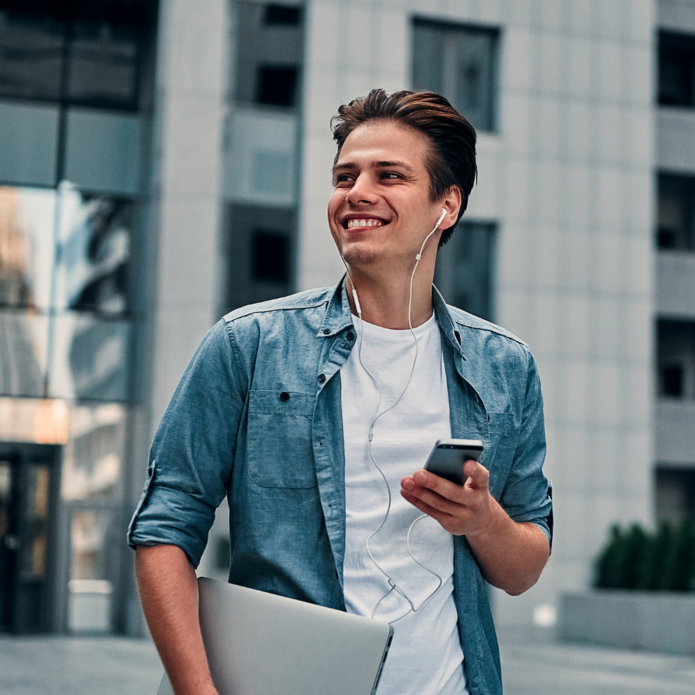 Uśmiechnięty chłopak w niebieskiej koszuli trzymający w ręku telefon komórkowy