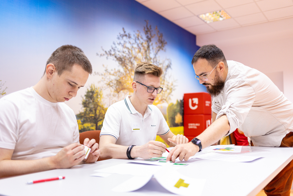 dwoje studentów siedzących przy stole dyskutuje z trenerem